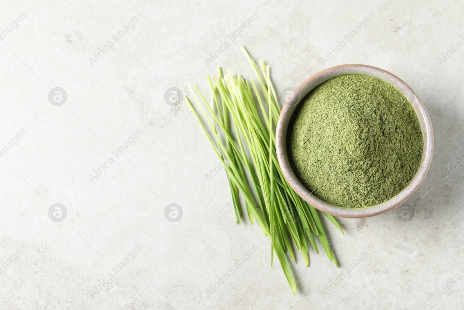 Photo of Wheat grass powder in bowl and fresh sprouts on light table, flat lay. Space for text