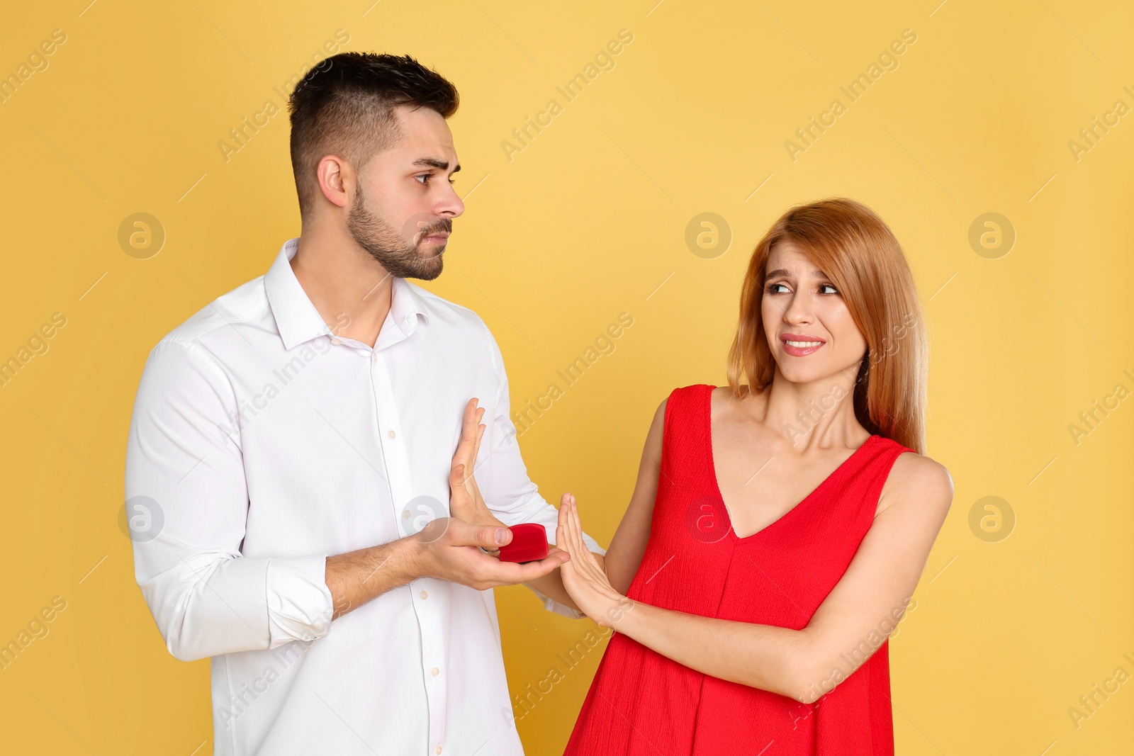 Photo of Young woman rejecting engagement ring from boyfriend on yellow background