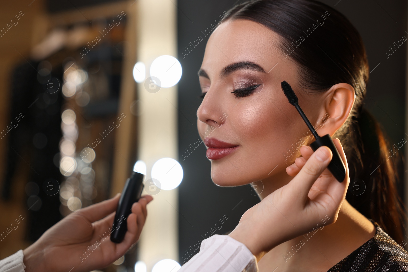 Photo of Makeup artist working with beautiful woman in dressing room, closeup