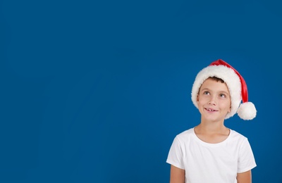 Little child in Santa hat dreaming on blue background, space for text. Christmas celebration