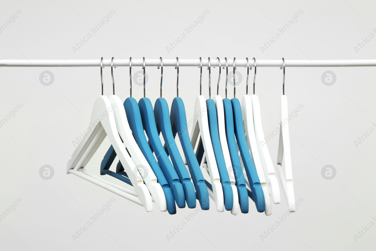 Photo of Empty clothes hangers on metal rail against light background