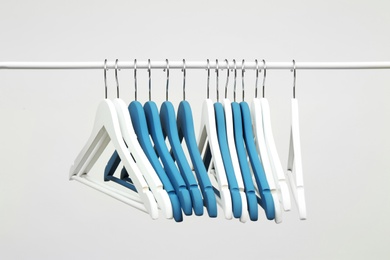 Photo of Empty clothes hangers on metal rail against light background