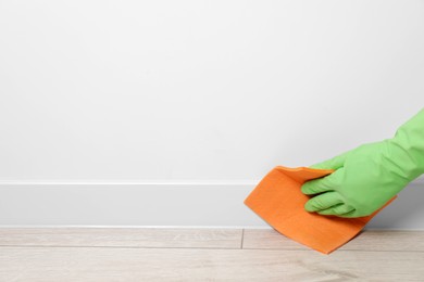 Woman in protective glove cleaning plinth with sponge cloth indoors, closeup. Space for text