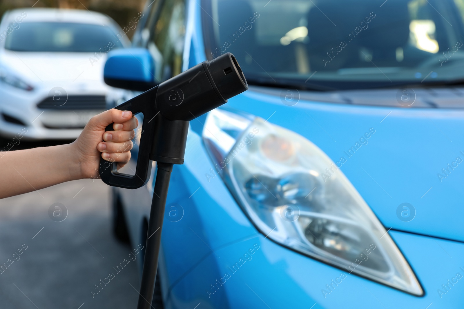 Photo of Woman holding power supply cable at electric vehicle charging station, closeup