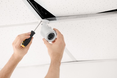 Technician installing CCTV camera on ceiling indoors, closeup