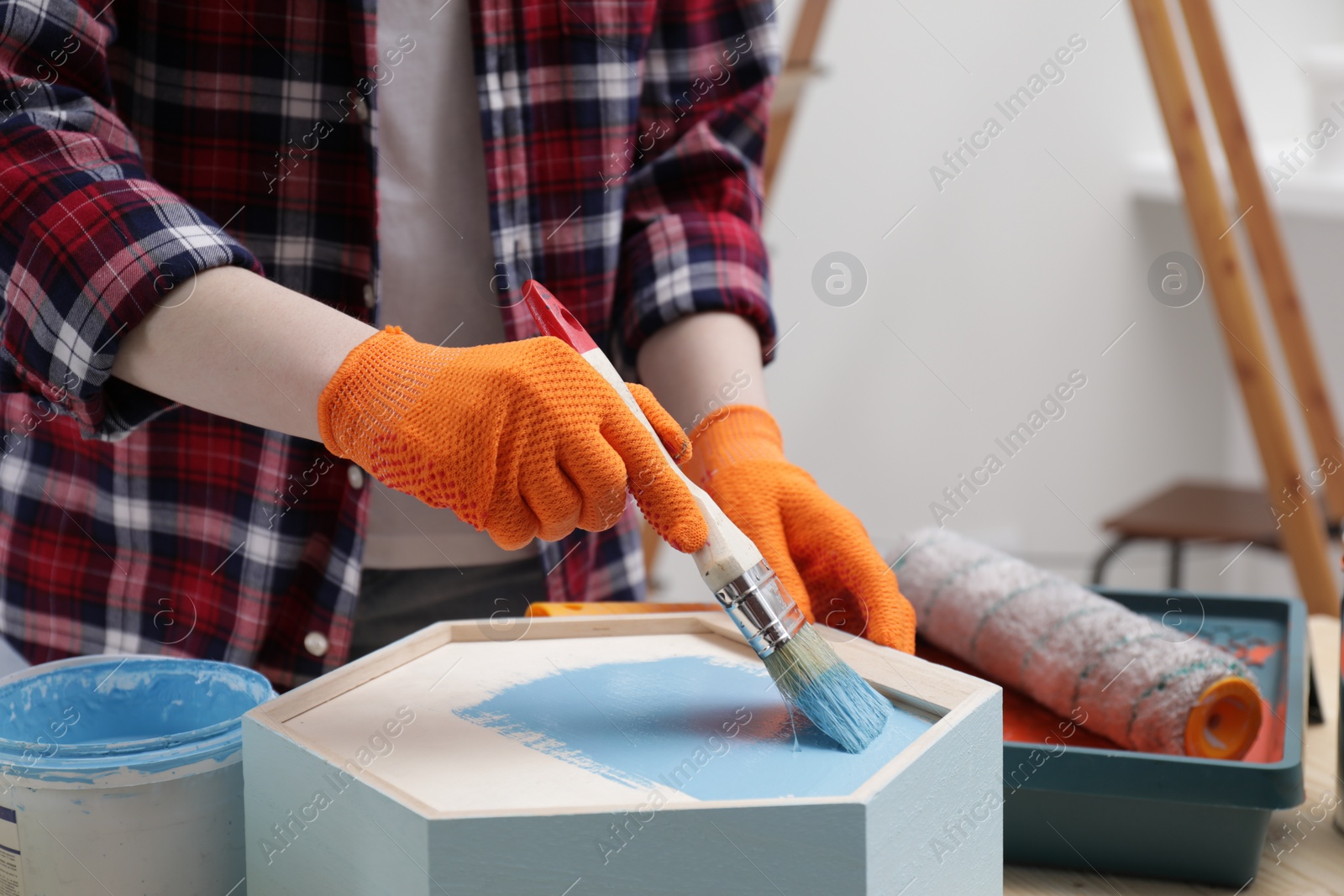 Photo of Woman painting honeycomb shaped shelf with brush at table indoors, closeup