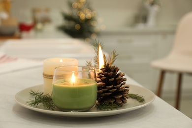 Photo of Burning scented conifer candles and pine cone on white table