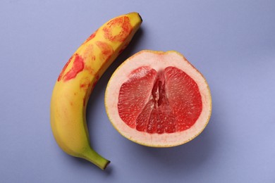 Photo of Banana with red lipstick marks and half of grapefruit on violet background, flat lay. Sex concept