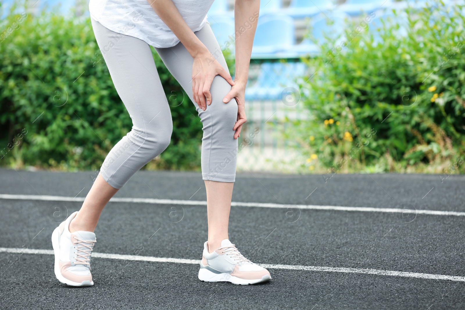 Photo of Woman in sportswear suffering from knee pain at stadium, closeup