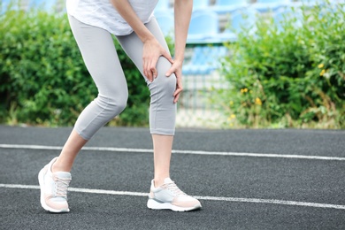 Photo of Woman in sportswear suffering from knee pain at stadium, closeup