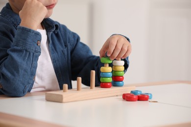 Photo of Little boy playing with stacking and counting game at table indoors, closeup. Child's toy