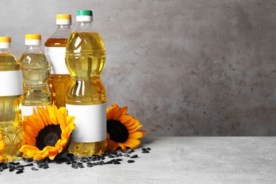 Photo of Bottles of sunflower cooking oil, seeds and yellow flowers on light grey table, space for text