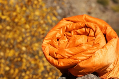 Photo of Orange sleeping bag on rock outdoors, space for text. Camping equipment