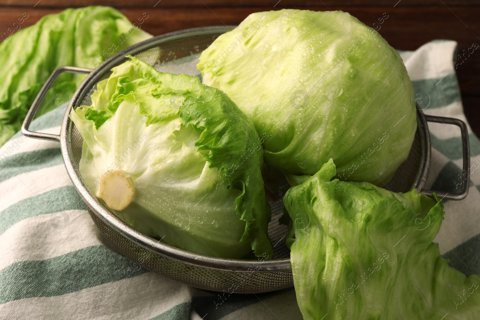 Photo of Colander with fresh green iceberg lettuce heads on table, closeup