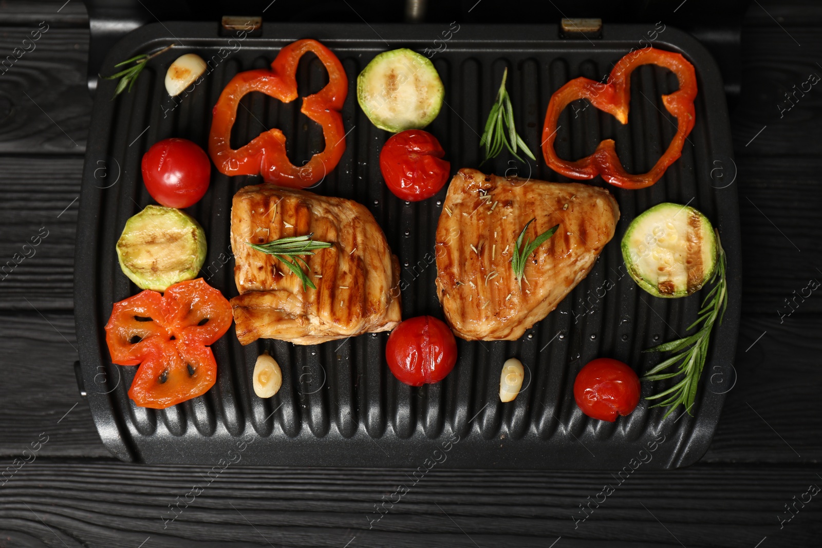 Photo of Electric grill with tasty meat, spices and vegetables on black wooden table, top view