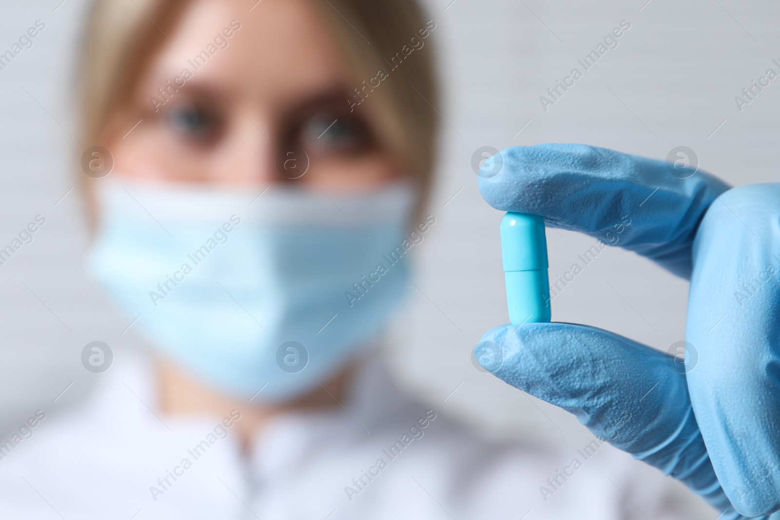 Photo of Doctor holding pill on light background, selective focus. Space for text