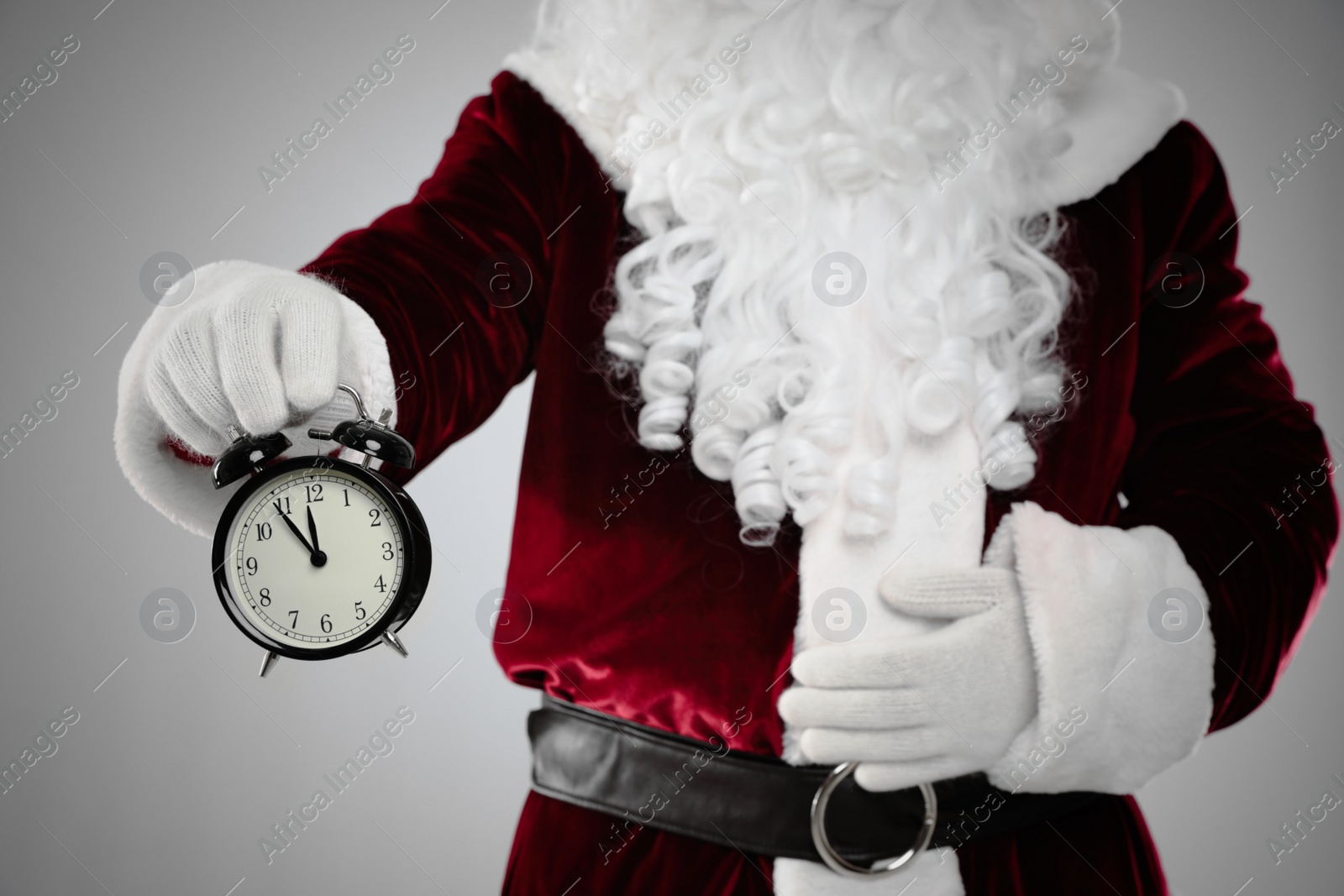 Photo of Santa Claus holding alarm clock on light grey background, closeup. Christmas countdown