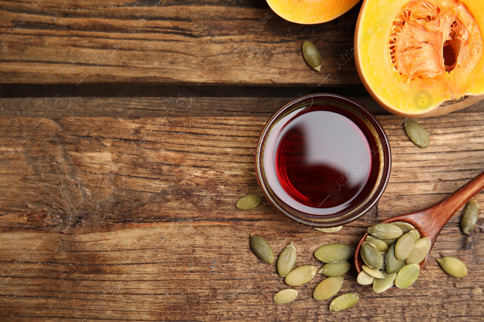 Photo of Glass bowl of oil and pumpkin seeds on wooden table, flat lay. Space for text