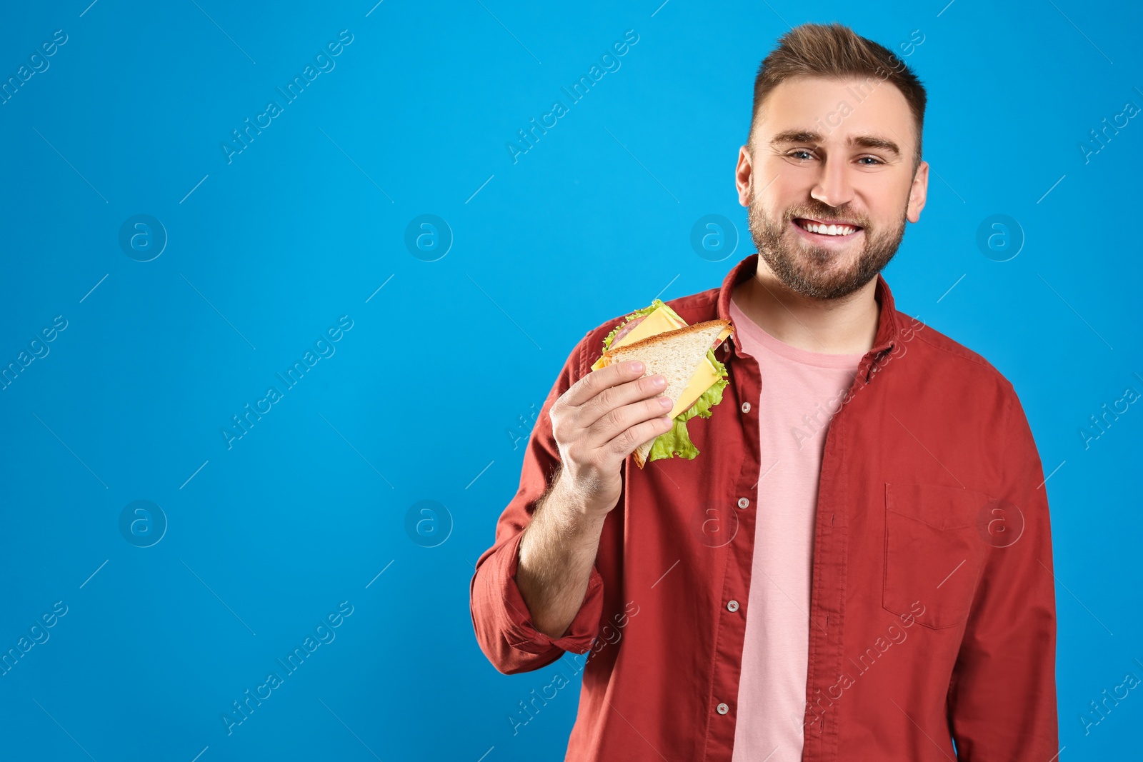 Photo of Young man with tasty sandwich on light blue background. Space for text