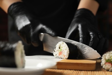 Photo of Chef in gloves cutting sushi roll at table, closeup