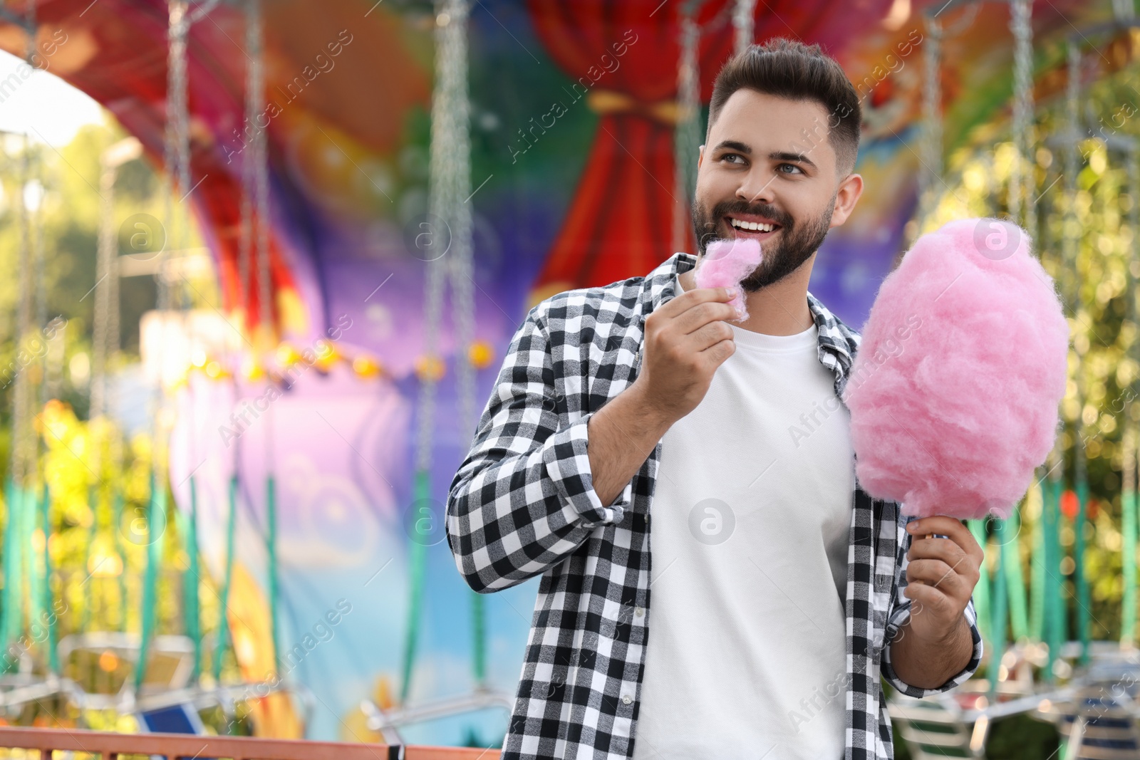 Photo of Happy young man eating cotton candy at funfair, space for text