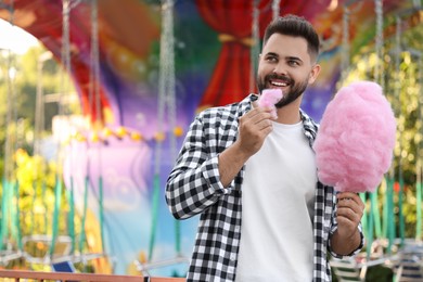 Photo of Happy young man eating cotton candy at funfair, space for text