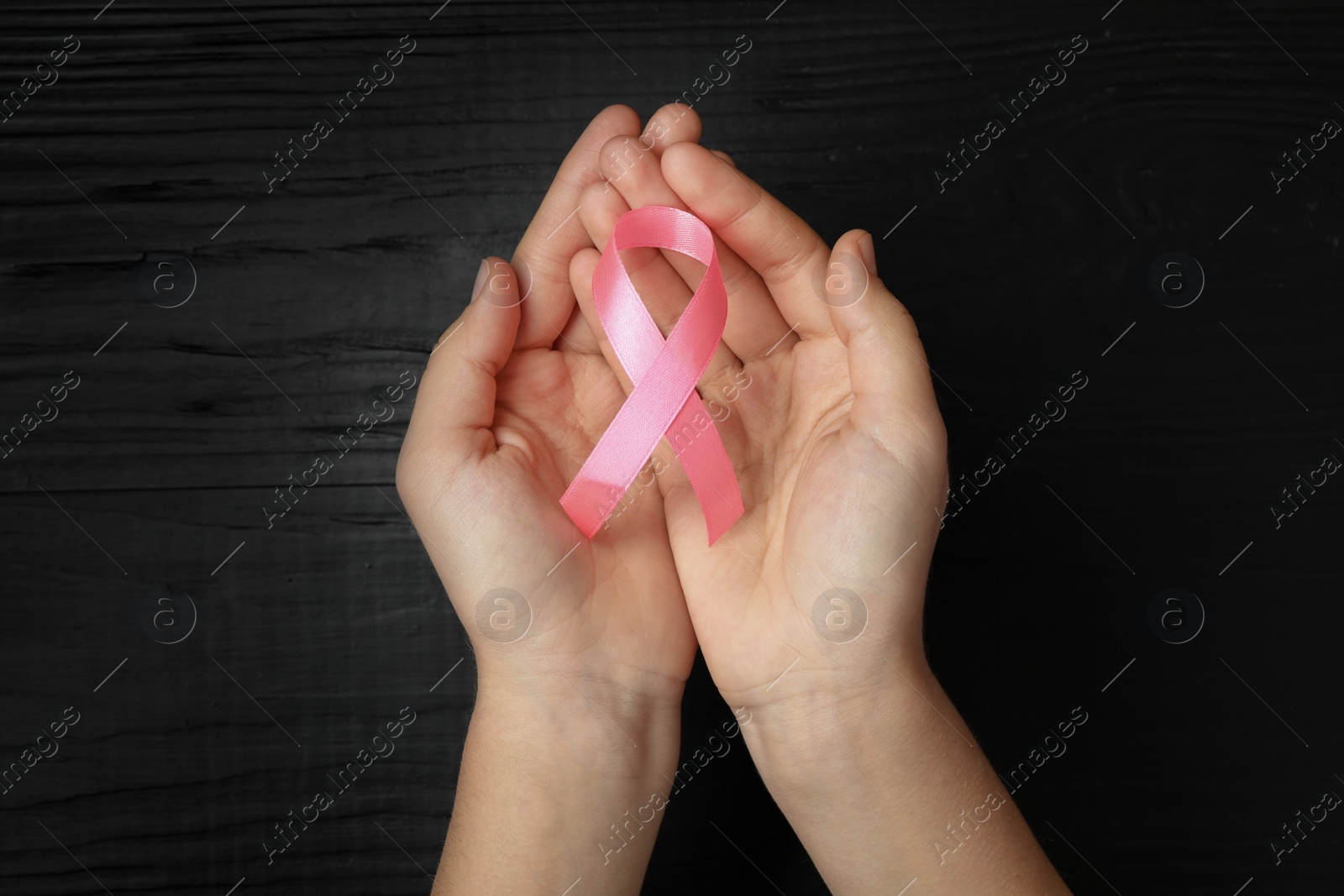 Photo of Young woman holding pink ribbon on wooden background, top view. Breast cancer concept