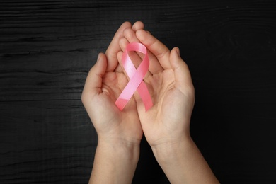 Photo of Young woman holding pink ribbon on wooden background, top view. Breast cancer concept