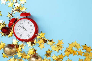 Alarm clock and festive decor on light blue background, flat lay with space for text. New Year countdown