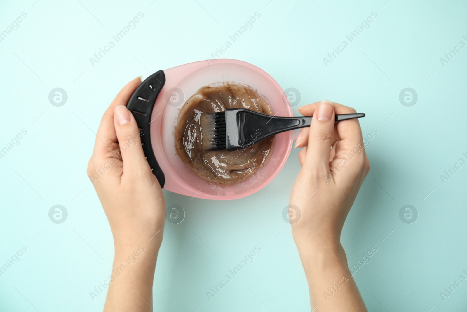 Photo of Woman preparing dye for hair coloring on light blue background, top view