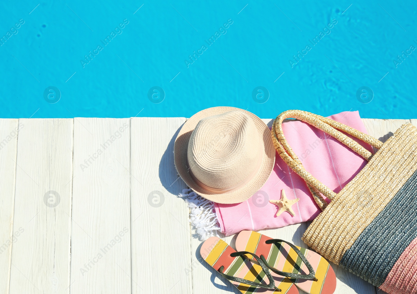 Photo of Beach accessories on wooden deck near swimming pool, top view. Space for text