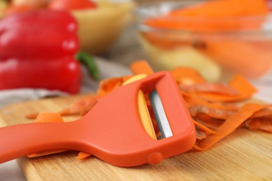 Photo of Wooden board with carrot peels and peeler on table, closeup