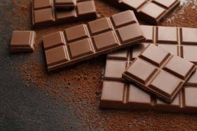 Delicious milk chocolate and cocoa powder on grey table, closeup
