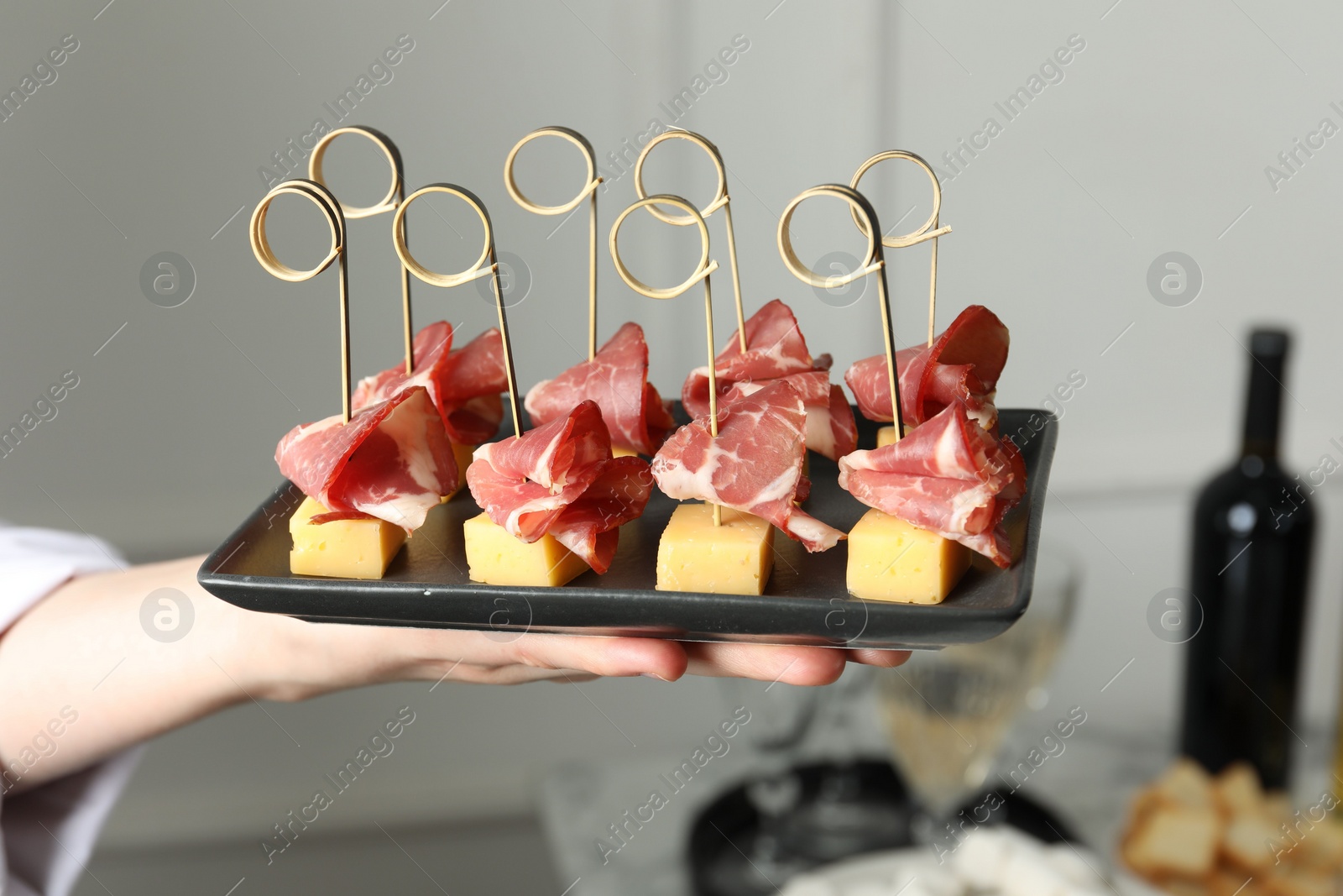 Photo of Woman holding plate of tasty canapes with ham and cheese indoors, closeup