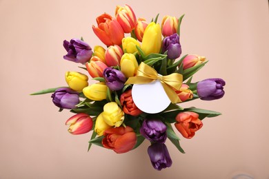 Bouquet of beautiful colorful tulips with blank card on beige background, top view. Birthday celebration