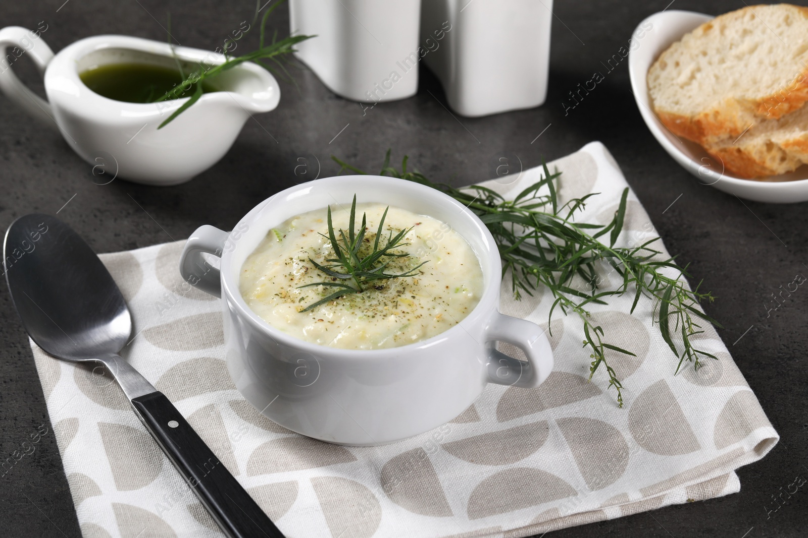 Photo of Delicious cream soup with tarragon, spices and potato in bowl served on dark textured table