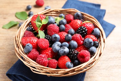 Many different fresh ripe berries in wicker basket on wooden table, closeup