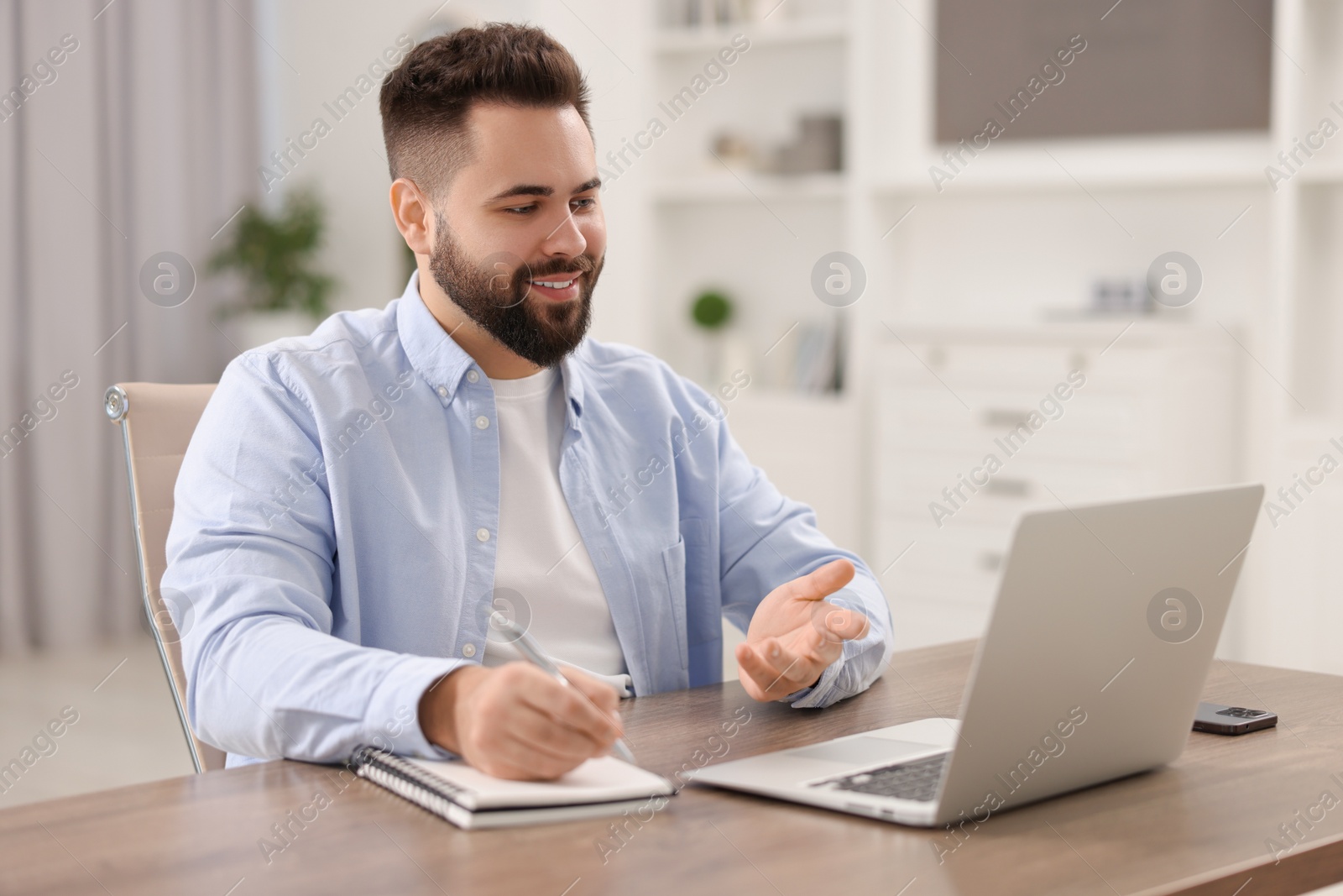 Photo of Young man using video chat during webinar at table in room