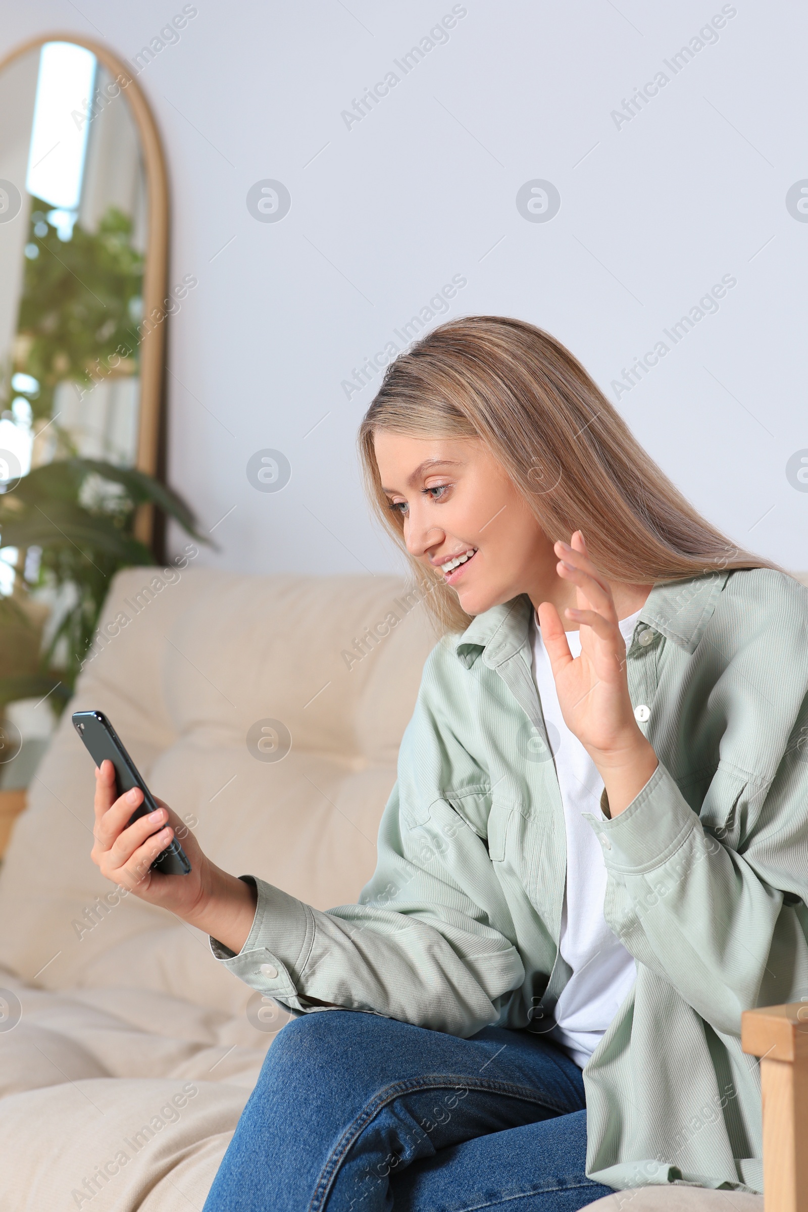 Photo of Woman with smartphone having video chat on sofa at home