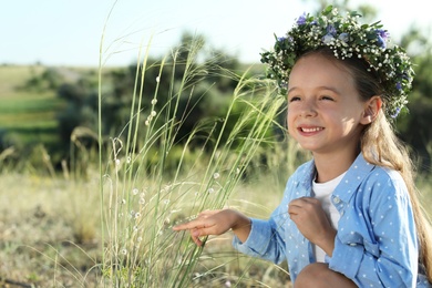 Cute little girl wearing flower wreath outdoors. Child spending time in nature