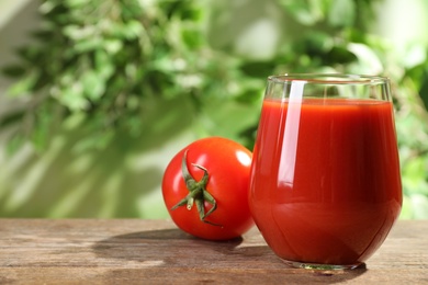 Delicious juice in glass and fresh tomato on wooden table against blurred background, space for text