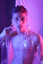 Stylish young man wearing clear coat and glasses in neon lights