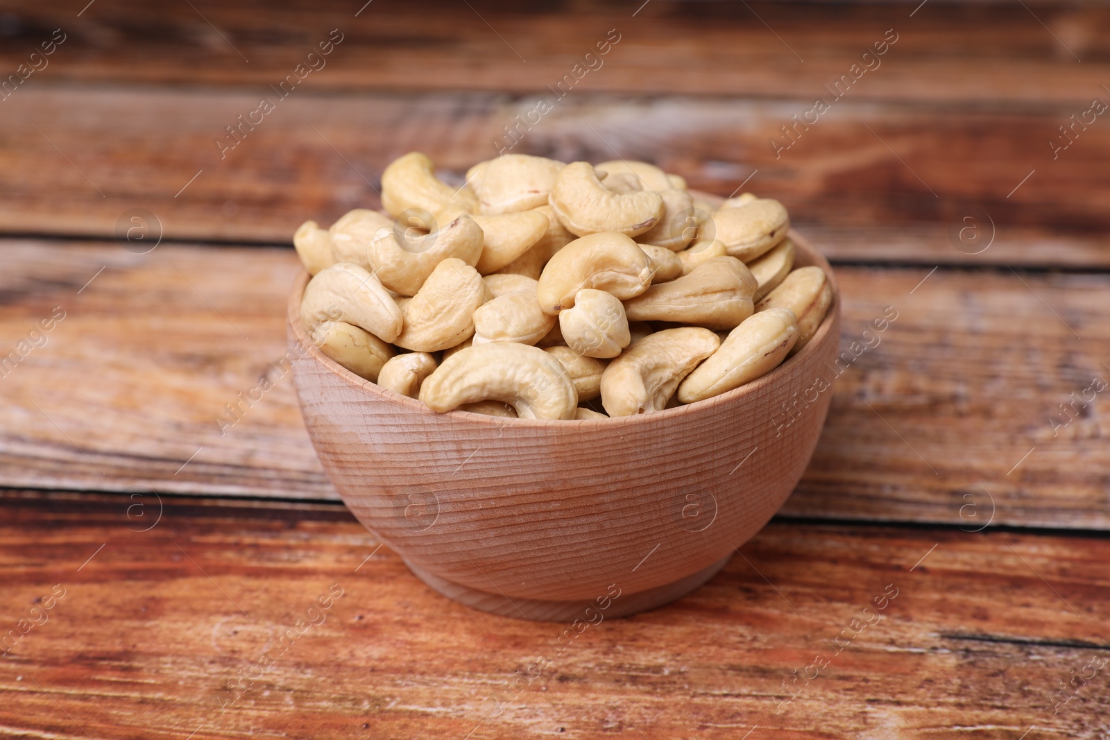 Photo of Tasty cashew nuts in bowl on wooden table