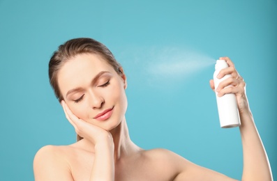 Photo of Young woman applying thermal water on face against color background. Cosmetic product