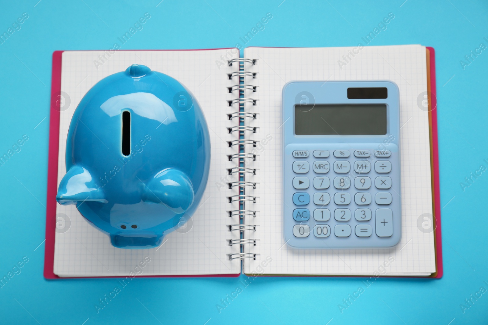 Photo of Piggy bank, notebook and calculator on light blue background, top view