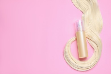 Photo of Spray bottle with thermal protection and lockblonde hair on pink background, flat lay. Space for text