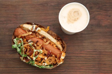 Fresh delicious hot dog and paper cup of coffee on wooden table, flat lay