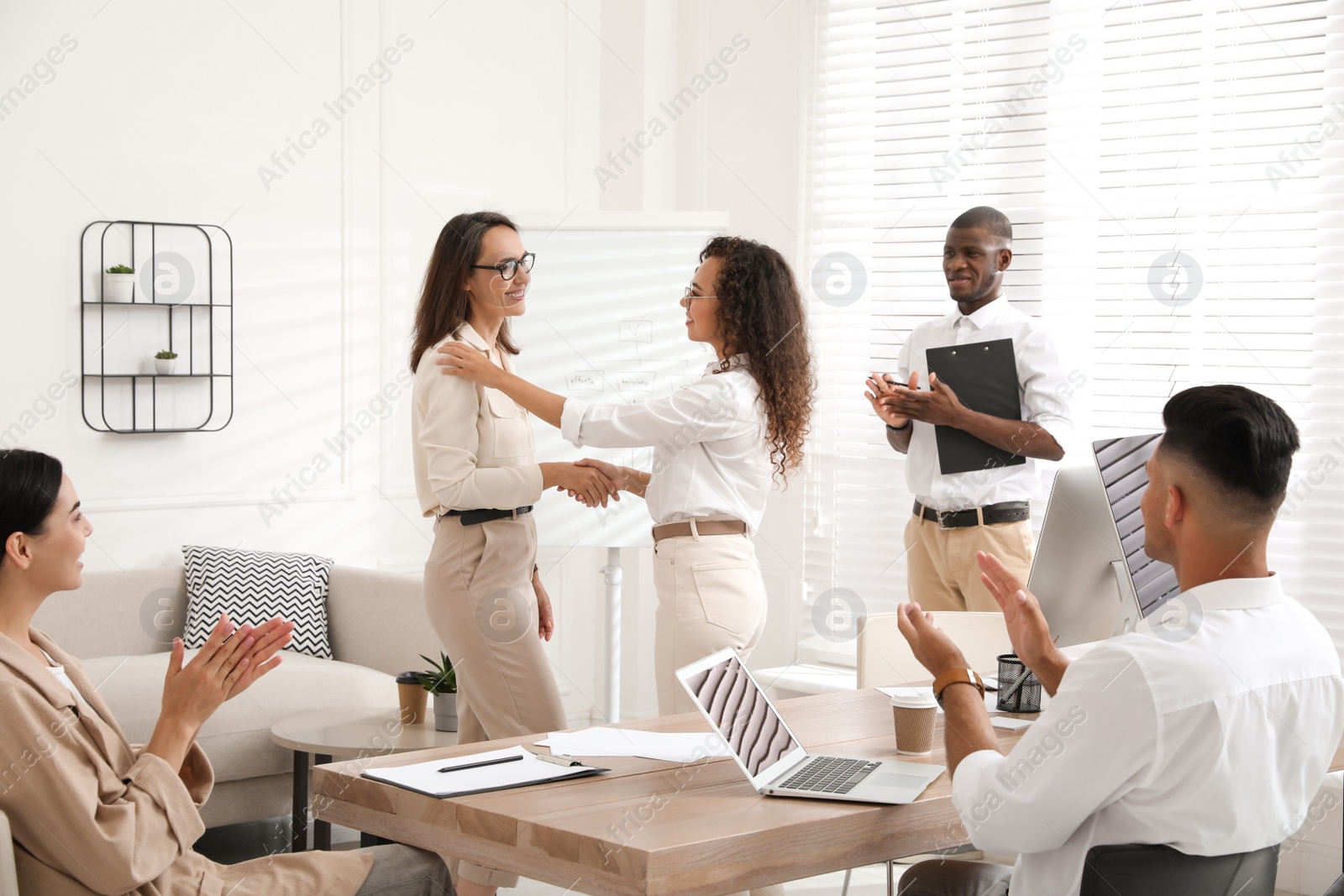 Photo of Boss shaking hand with new employee and coworkers applauding in office