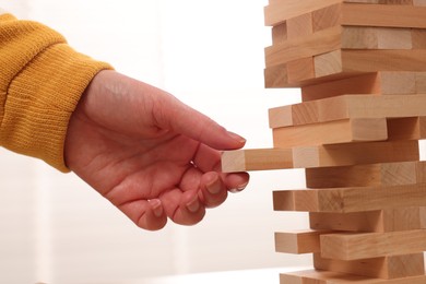 Photo of Playing Jenga. Woman removing wooden block from tower, closeup
