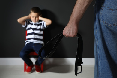 Man threatening his son with belt indoors, closeup. Domestic violence concept